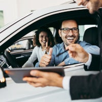 Couple in new car giving thumbs up to salesman